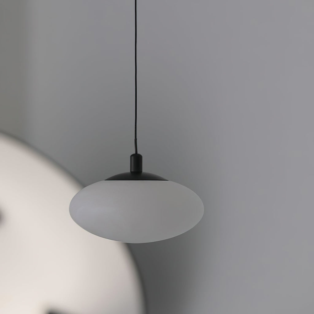 Unlit Clérachic Mini Discus pendant light against a soft grey wall, smooth alabaster shade under a matte black cap.
