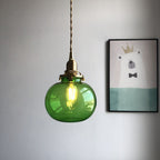 Green Clérachic Mini Glass Pendant Light, a smooth flattened oval lit to bright emerald against a plain grey wall.