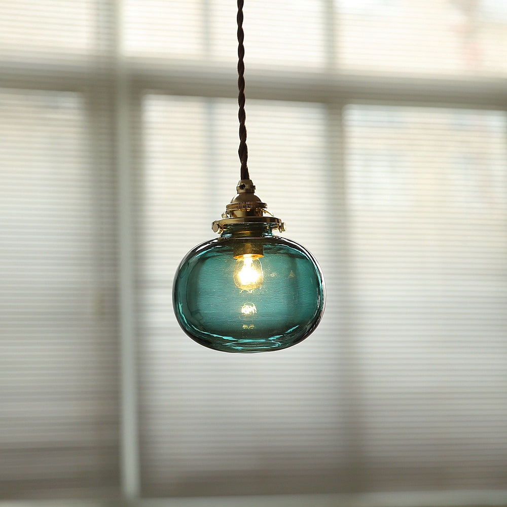 Clérachic Mini Glass Pendant Light in Blackish Green, lifted to a clear aqua by the daylight through the blind behind it.