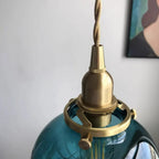 Detail of the Clérachic Mini Glass Pendant Light's brass-finish holder and twisted fabric flex clamped over the teal glass.