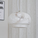 Clérachic alabaster pendant unlit beside a lace curtain, natural stone reading soft cream.