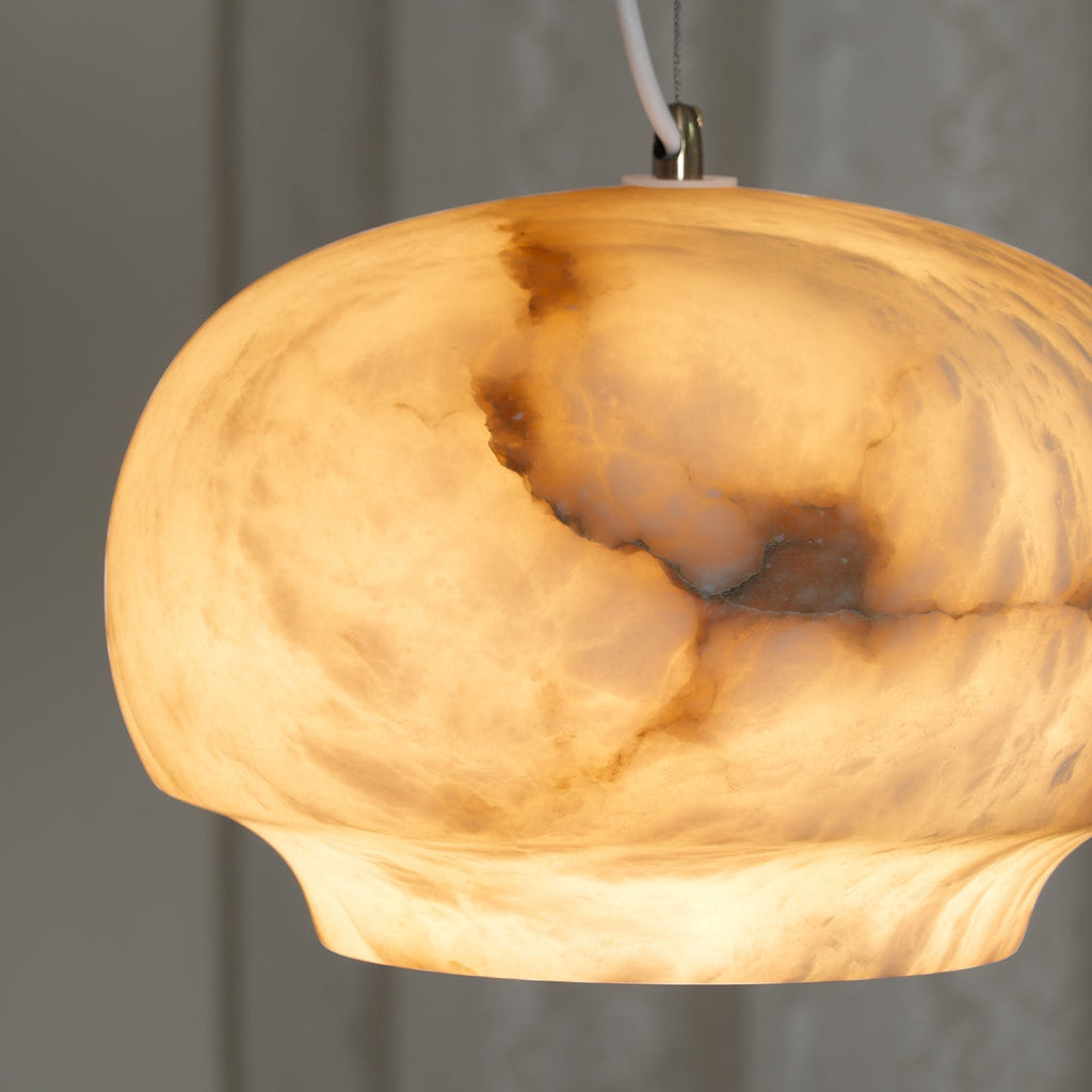 The Clérachic alabaster pendant lit close, warm amber light pooling through the stone's veining.