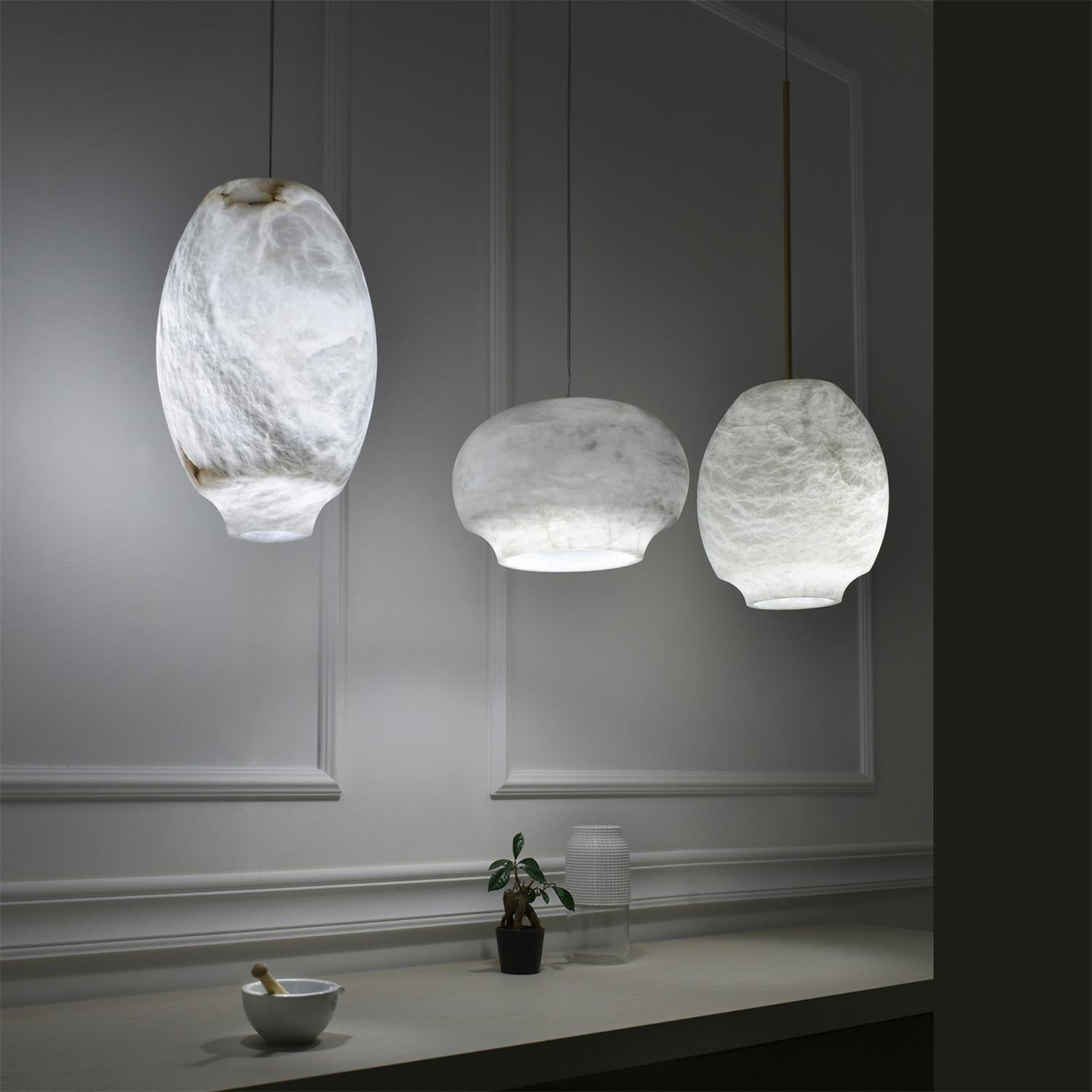 Three Clérachic alabaster pendants at staggered heights in a dark grey panelled room.