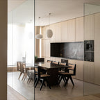 Clérachic alabaster pendants seen through a glass partition above a long timber dining table.