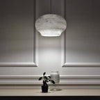 The Clérachic alabaster pendant lit above a console with a small potted plant and glass vase.