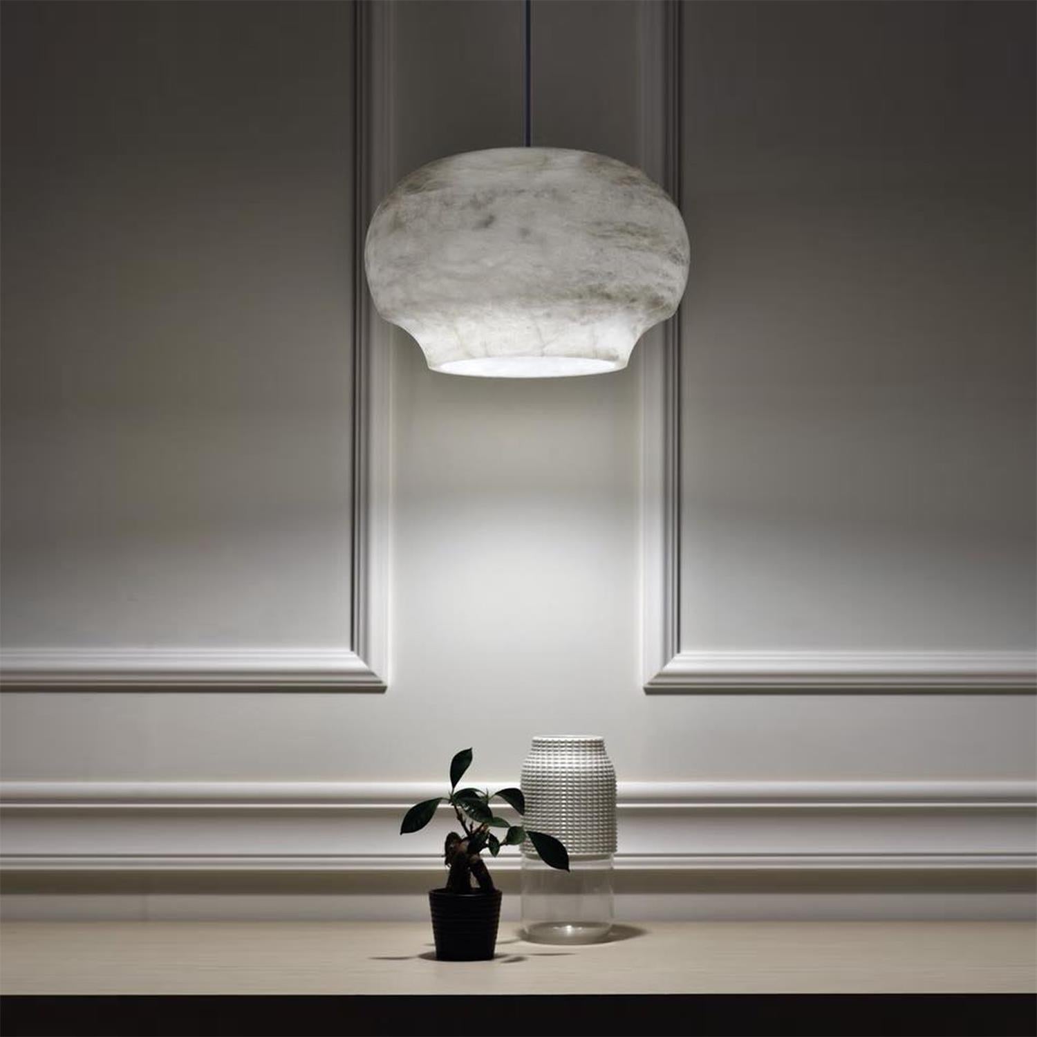 The Clérachic alabaster pendant lit above a console with a small potted plant and glass vase.