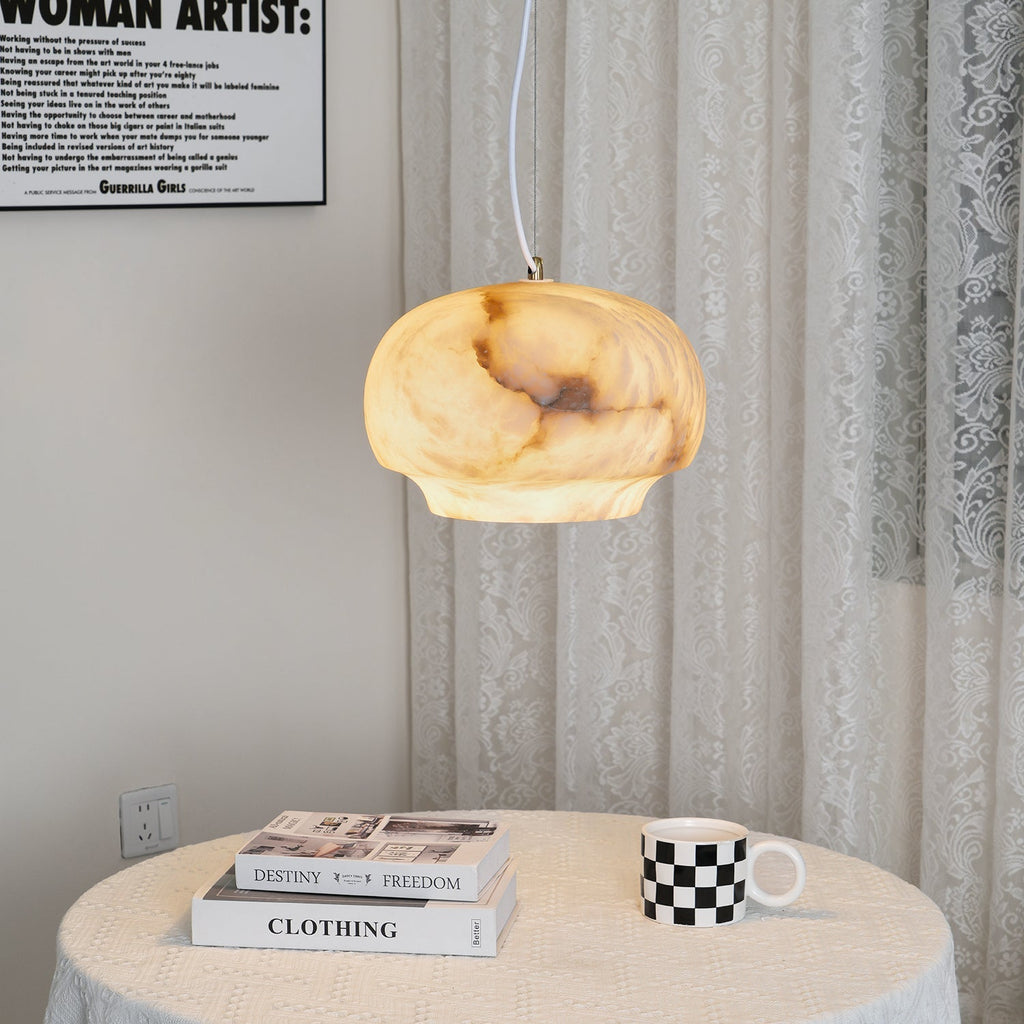 Clérachic alabaster pendant lit over a round cloth-covered table set with books and a mug.