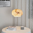 Clérachic alabaster pendant lit over a round cloth-covered table set with books and a mug.