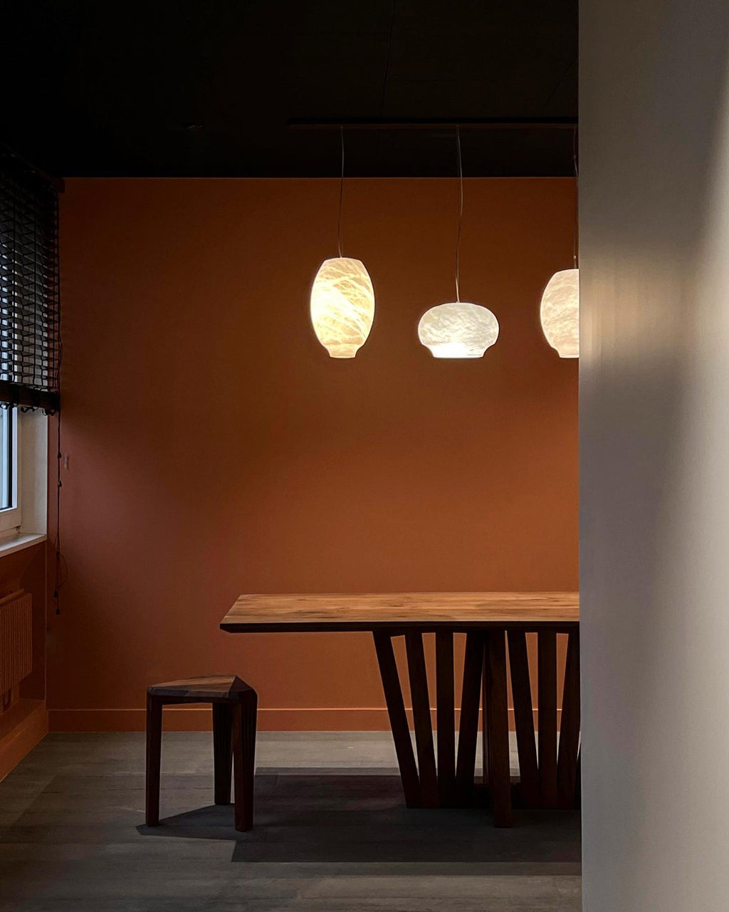 Three Clérachic alabaster pendants lit in a rust-walled dining room above a wooden table.