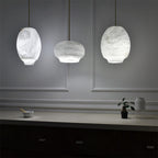 Three Clérachic alabaster pendants lit against a grey panelled wall above a low ledge.