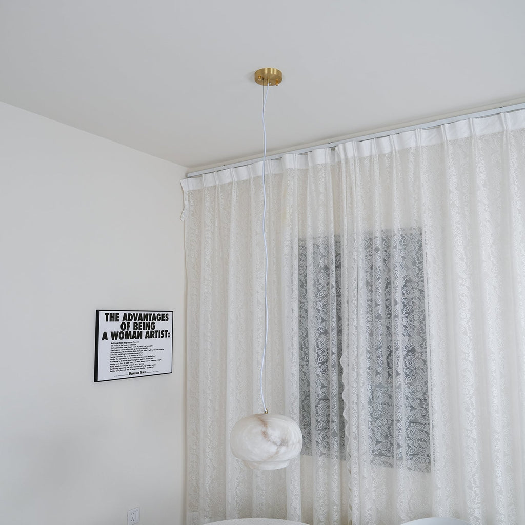 The Clérachic alabaster pendant hung in a bright white room against a sheer lace curtain.