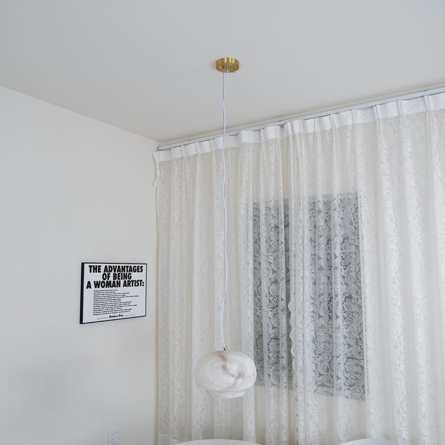 The Clérachic alabaster pendant hung in a bright white room against a sheer lace curtain.