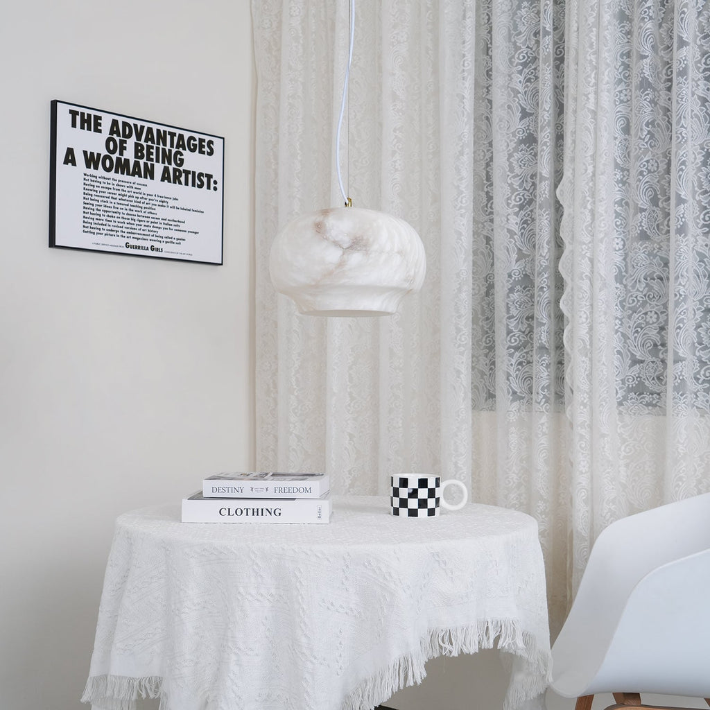 Clérachic alabaster pendant lit over a round table laid with stacked books and a chequered mug.
