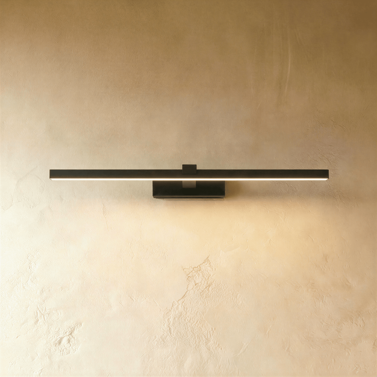 Clérachic slim black linear wall light in a longer length, lit along the diffuser on a warm textured limewash wall.