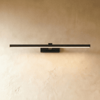 Clérachic slim black linear wall light in a longer length, glowing warmly on a textured plaster wall, with a small wall plate.