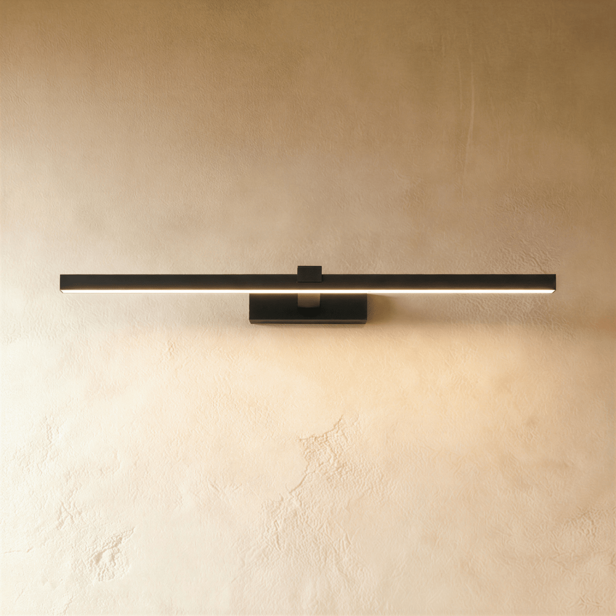 Clérachic slim black linear wall light in a longer length, glowing warmly on a textured plaster wall, with a small wall plate.