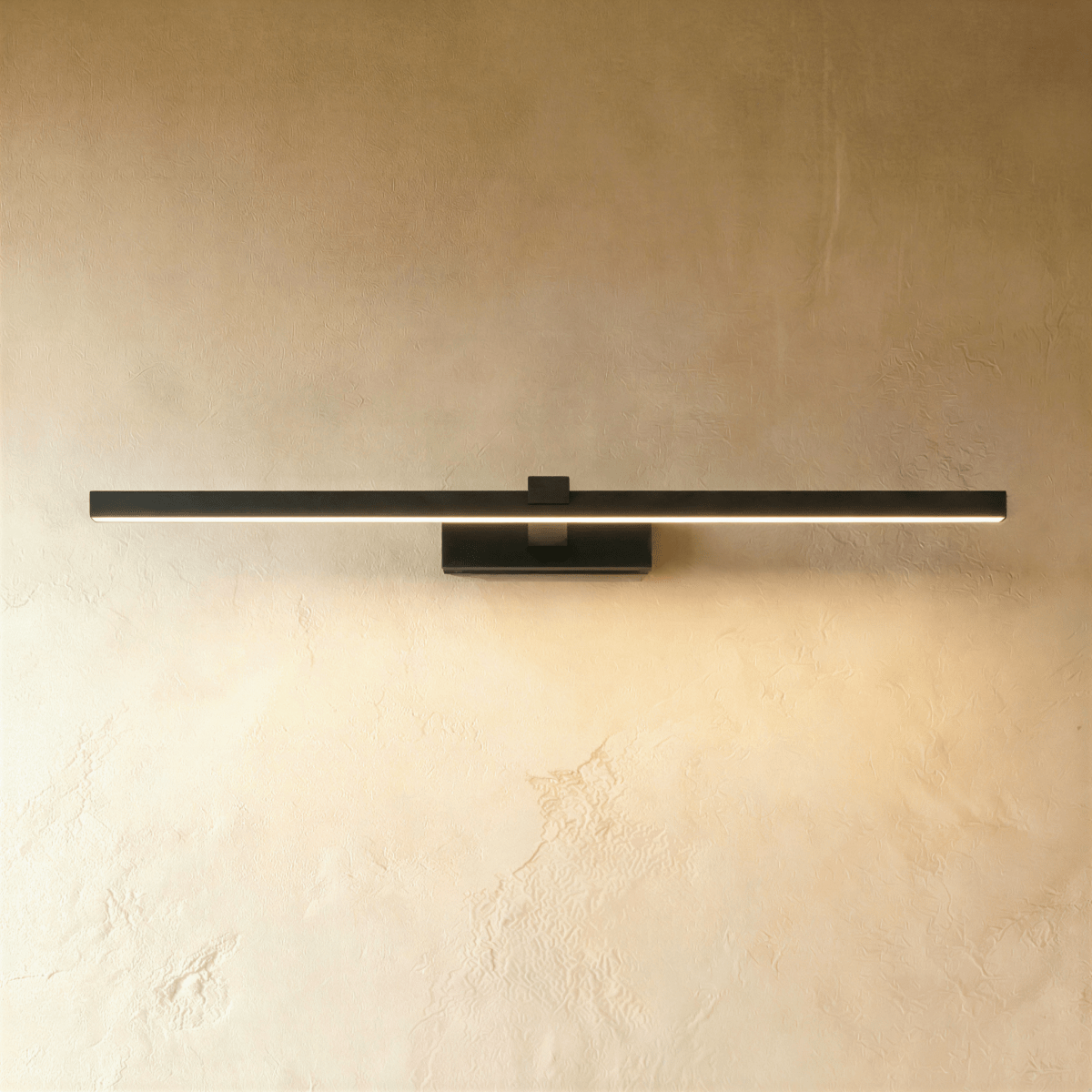 Clérachic slim black linear wall light in its longest length, lit along the diffuser on a textured limewash wall.