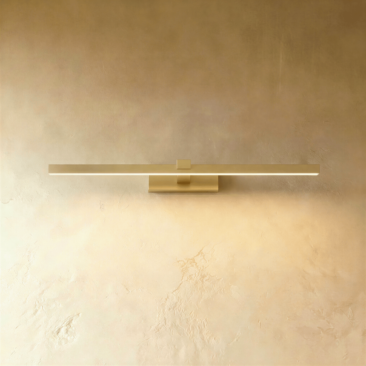 Clérachic slim brushed gold linear wall light in a longer length, lit warmly on a textured limewash wall.