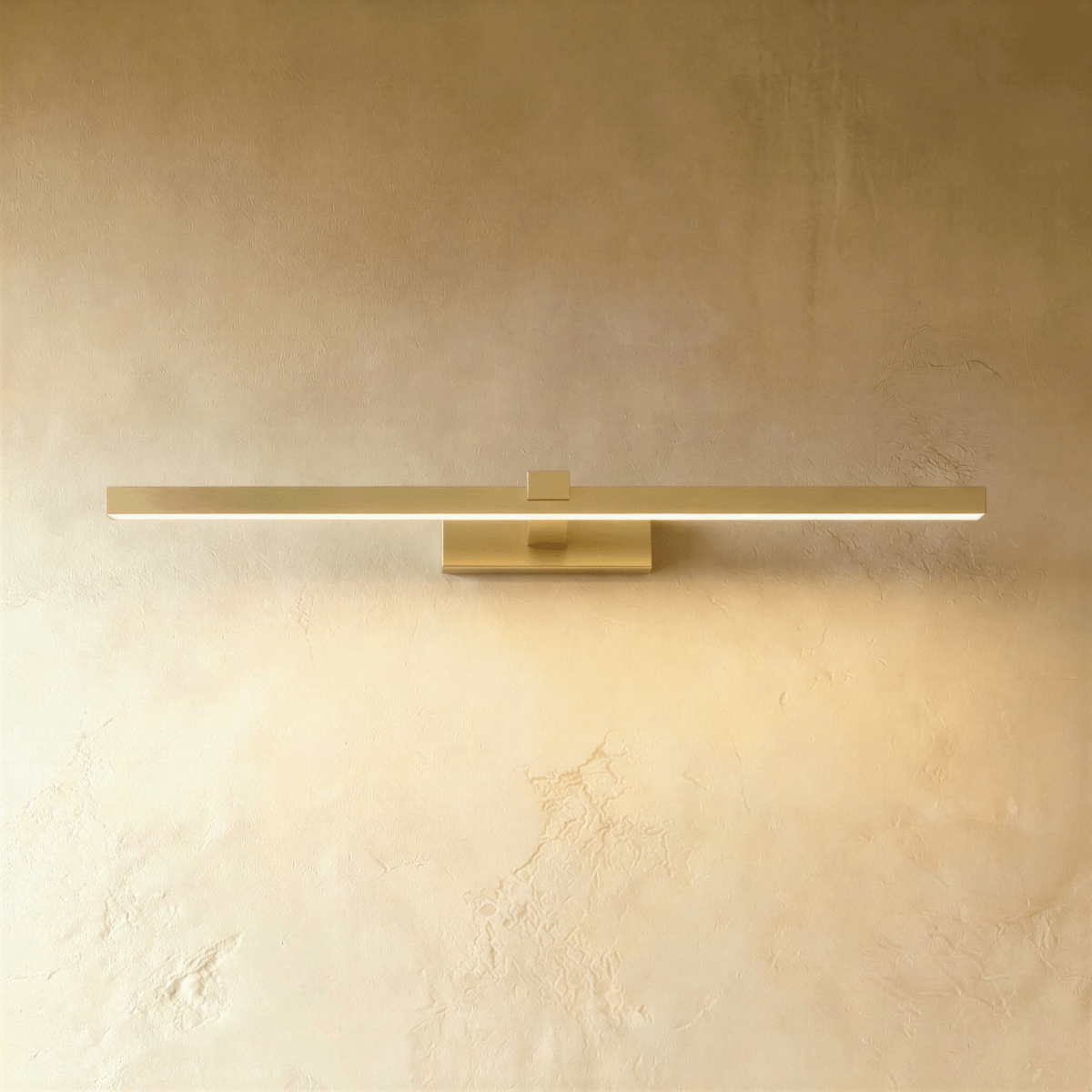 Clérachic slim brushed gold linear wall light in a longer length, glowing along the diffuser on a warm plaster wall.