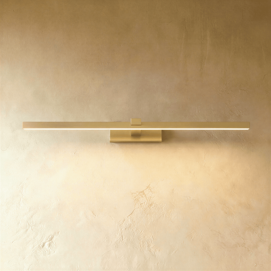 Clérachic slim brushed gold linear wall light in its longest length, lit along the diffuser on a textured limewash wall.