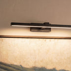 Close view of a Clérachic black linear wall light and its rectangular wall plate, lighting the top of a framed painting.