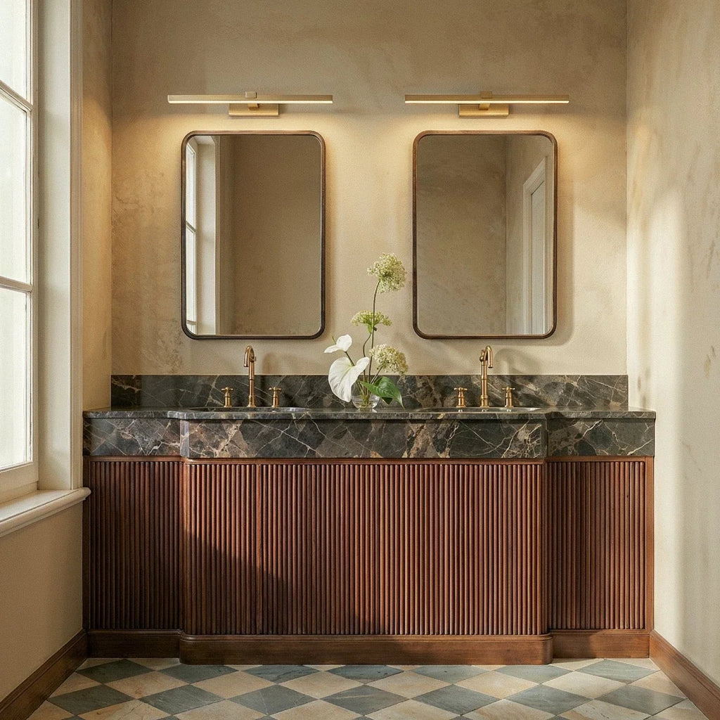 Clérachic gold linear wall lights above two framed mirrors over a marble double vanity with fluted wooden cabinets.