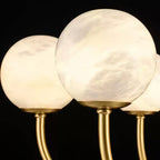 Close view of two Clérachic alabaster globes, each seated in a turned brass cup on its own arm.