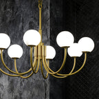 The Clérachic globe chandelier lit against a dark textured wall, stone shades glowing softly.