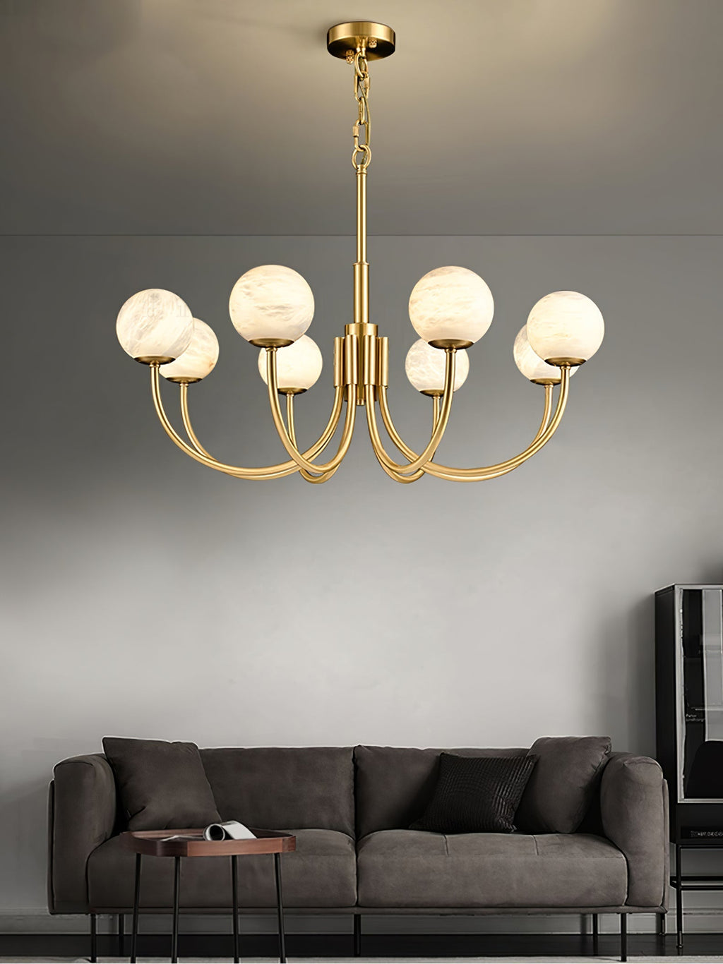The Clérachic globe chandelier hung above a dark grey sofa on a pale plaster wall.