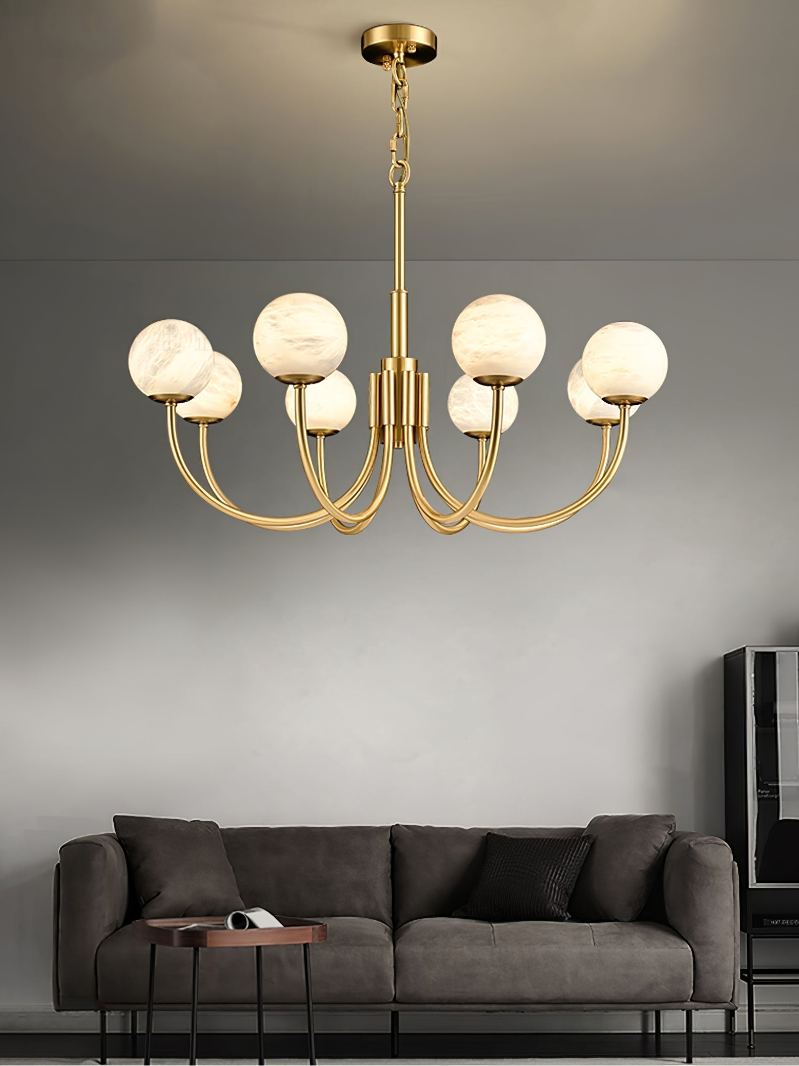 The Clérachic globe chandelier hung above a dark grey sofa on a pale plaster wall.