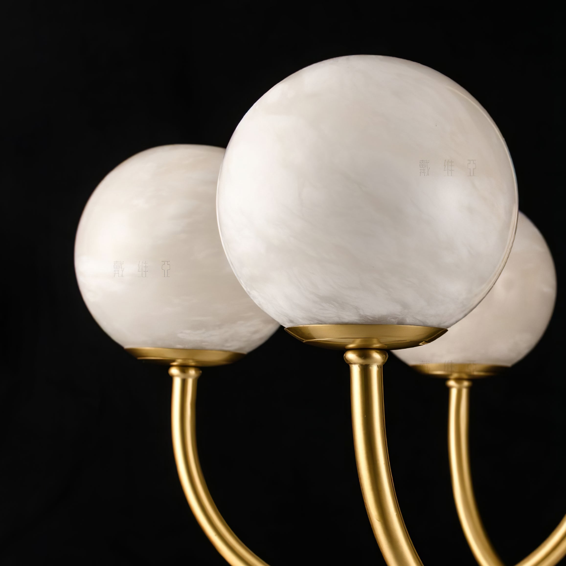 Macro of three Clérachic alabaster globes on black, the natural stone grain clearly visible.
