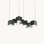A Clérachic chandelier of black cube-shaped lights at different angles, hung on thin wires against a plain off-white backdrop.