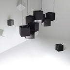 Cluster of black Clérachic cube lights hung at tilted angles in a white room, with loose black cubes on the walls and floor.
