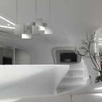 A Clérachic chandelier of white cubes seen from a distance in a curved white interior, with a branch in a vase to the right.