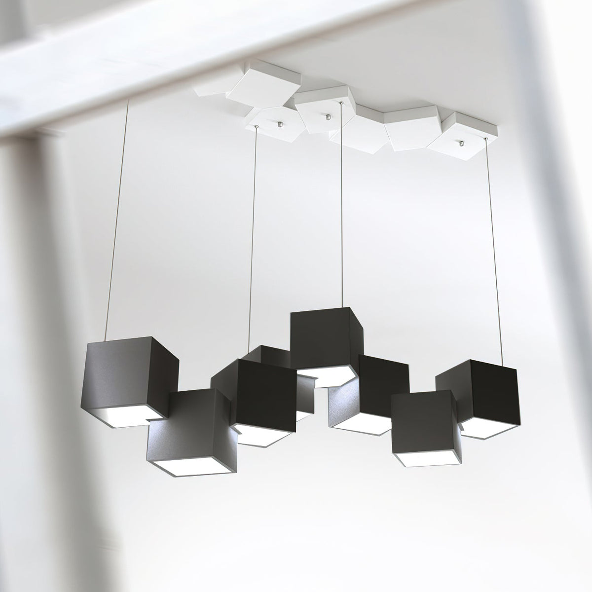Looking up at a Clérachic chandelier of black cubes on four wires, with a white tiled canopy of cubes on the ceiling above.