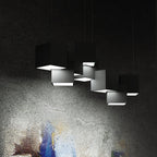 A Clérachic chandelier of black cubes against a dark textured wall, with white light glowing from the open underside of each cube.