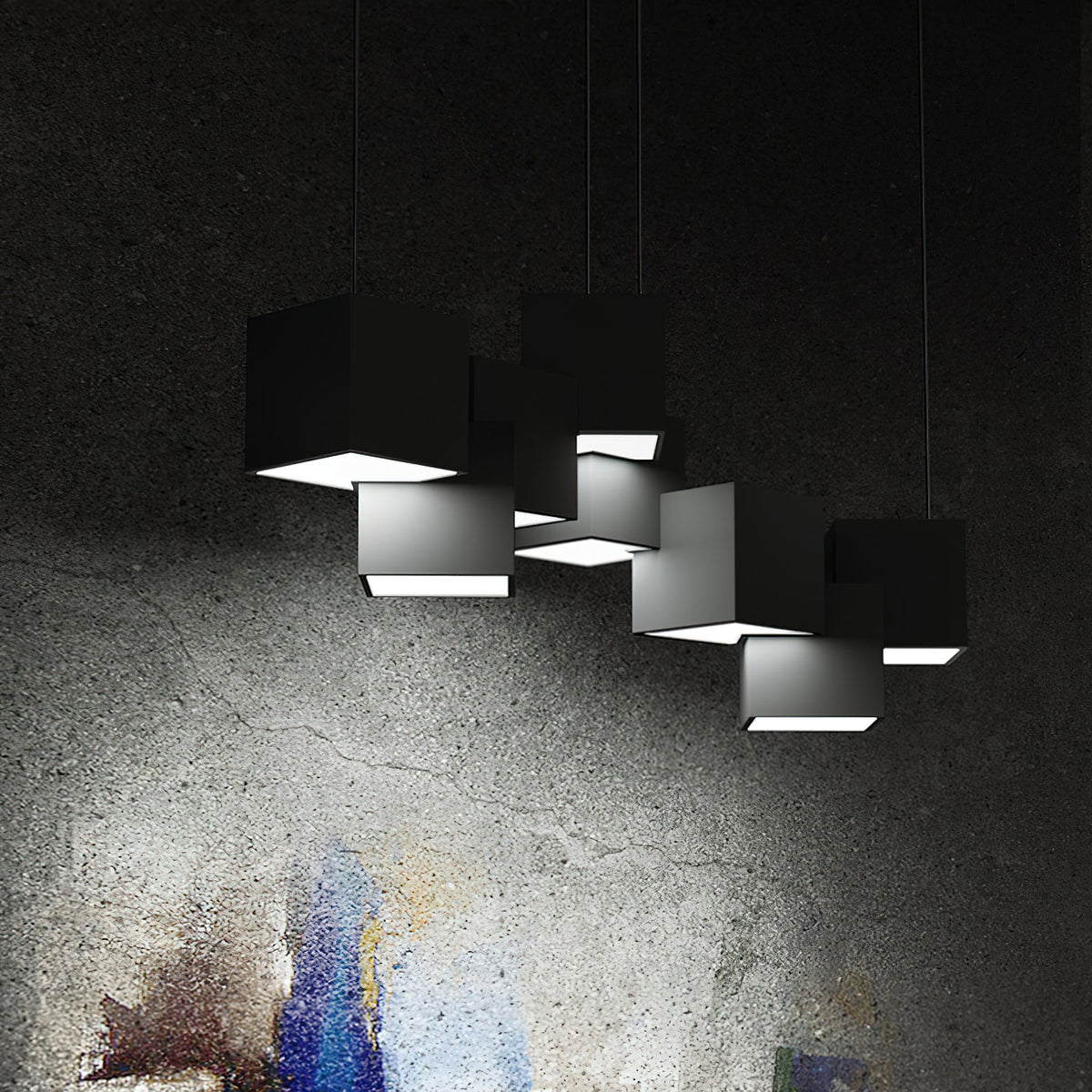 A Clérachic chandelier of black cubes against a dark textured wall, with white light glowing from the open underside of each cube.