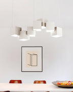 White Clérachic cube chandelier hung above a white dining table with a framed print and a bowl of fruit.