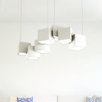 Clérachic chandelier of white cubes against a pale wall above a sofa with blue patterned cushions.