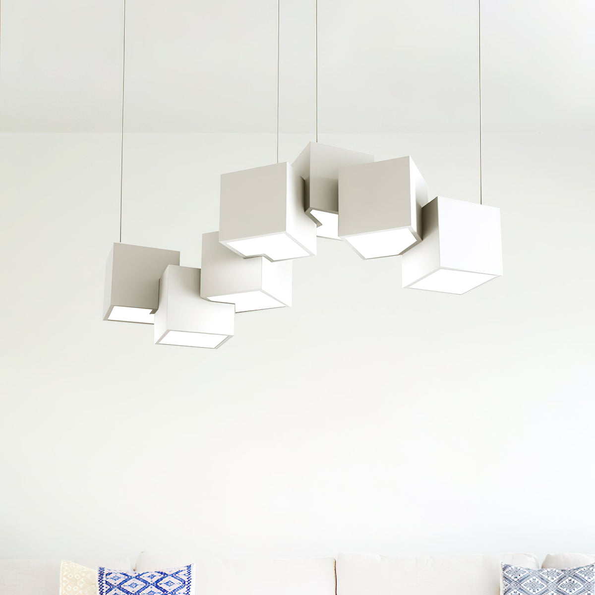 Clérachic chandelier of white cubes against a pale wall above a sofa with blue patterned cushions.