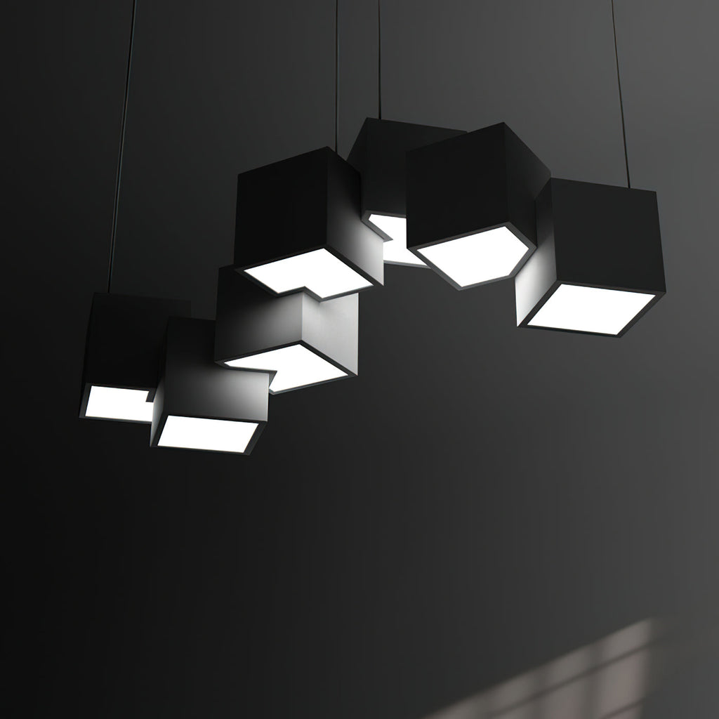 Clérachic black cube chandelier in a dark room, the bright undersides of the tilted cubes lighting the grey wall.