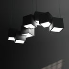 Clérachic black cube chandelier in a dark room, the bright undersides of the tilted cubes lighting the grey wall.