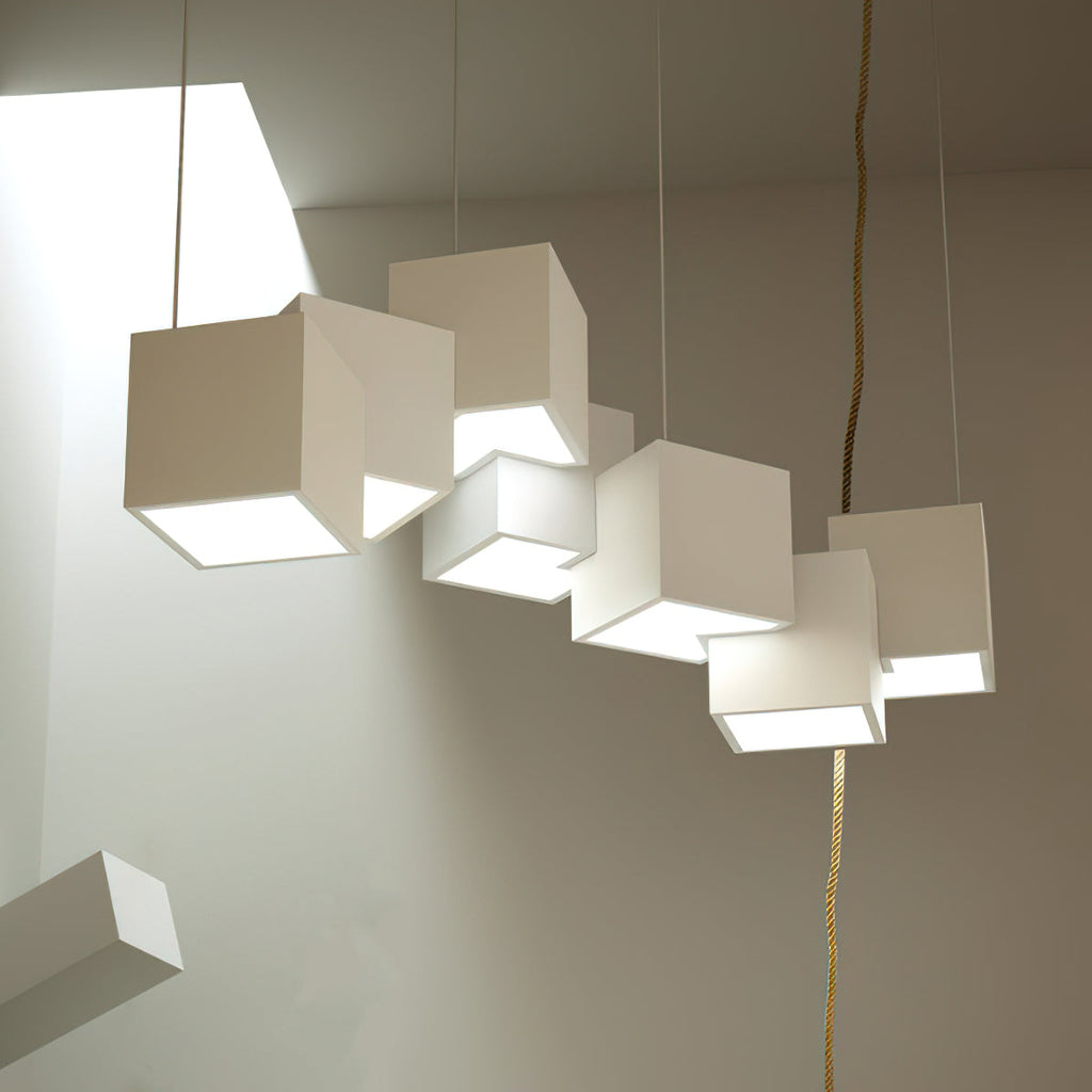 White Clérachic cube chandelier in a sunlit room, with a brass-coloured cord and a loose cube leaning in the corner.
