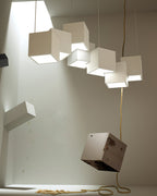 White Clérachic cubes hung from a high ceiling in a bright room, with a heavy cube and a rope hanging below.