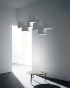 A Clérachic white cube chandelier in a grey room with a doorway and a round wooden coffee table with a bulb on it.
