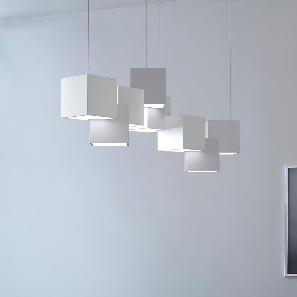 White Clérachic cube chandelier against a light blue-grey wall, the cubes stacked unevenly with a bright base to each.