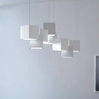 White Clérachic cube chandelier against a light blue-grey wall, the cubes stacked unevenly with a bright base to each.