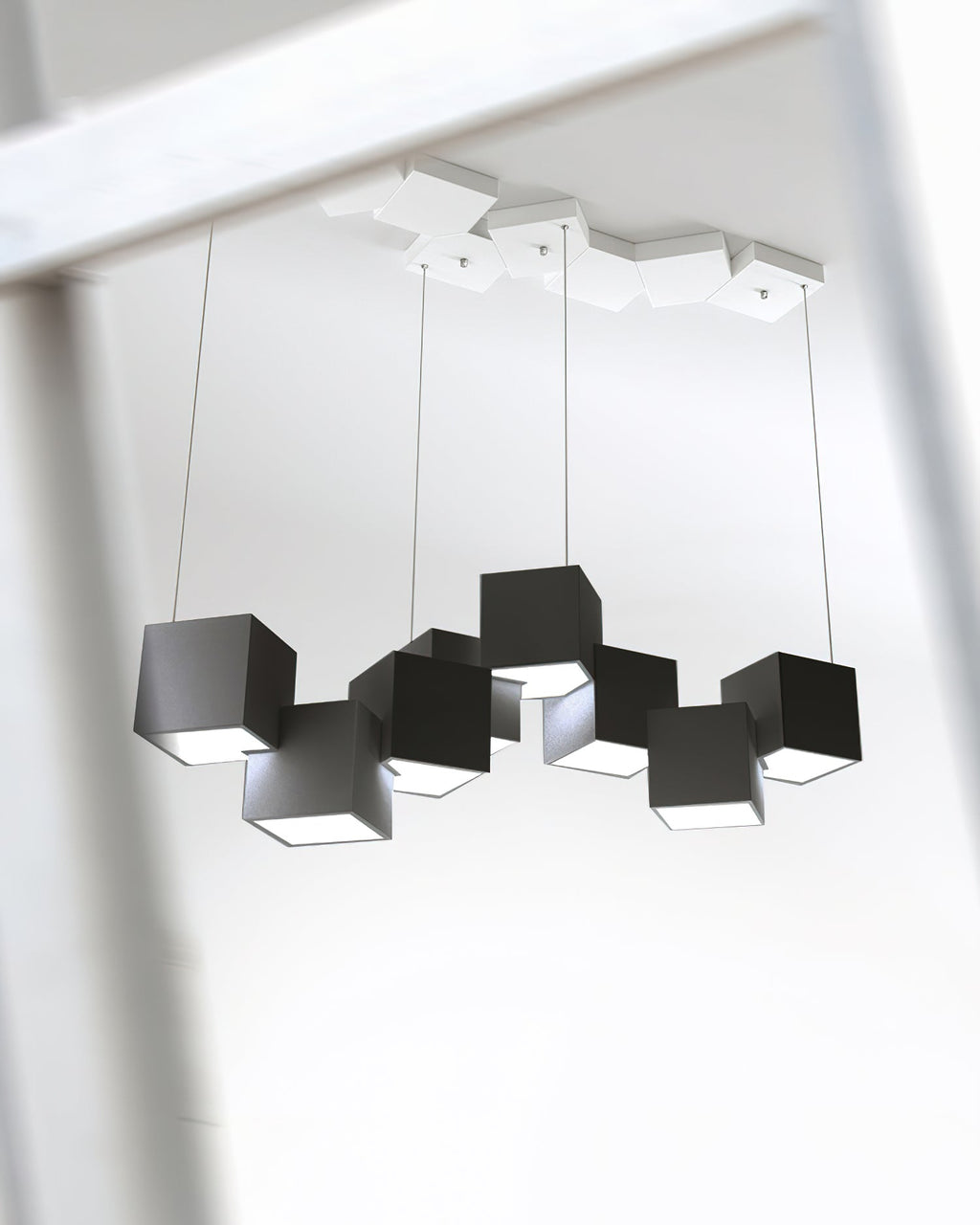 Looking up at a black Clérachic cube chandelier, with a white canopy of cubes at the ceiling and four thin wires.