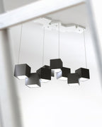 Looking up at a black Clérachic cube chandelier, with a white canopy of cubes at the ceiling and four thin wires.