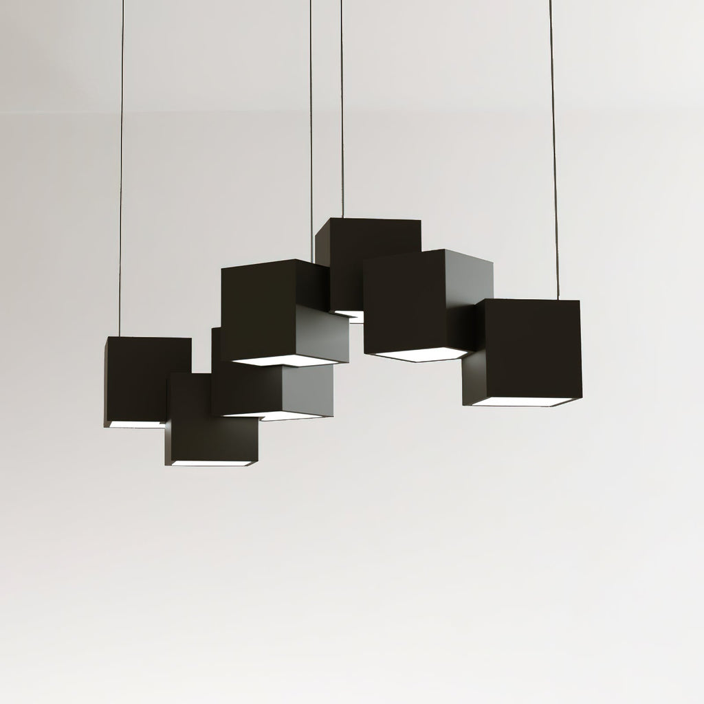 A Clérachic black cube chandelier against a pale wall, the cubes linked in an uneven row with lit undersides.